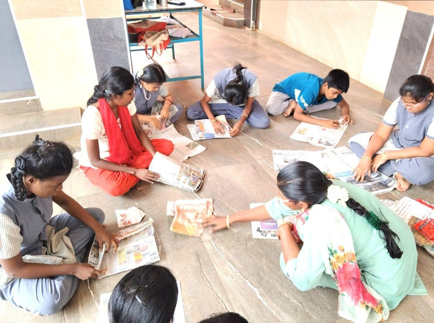 Students and a teacher sit together on the floor working on a paper craft activity