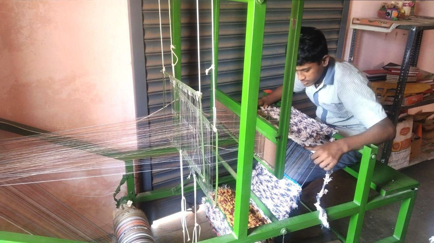 An older student weaves a mat on the school's green floor loom